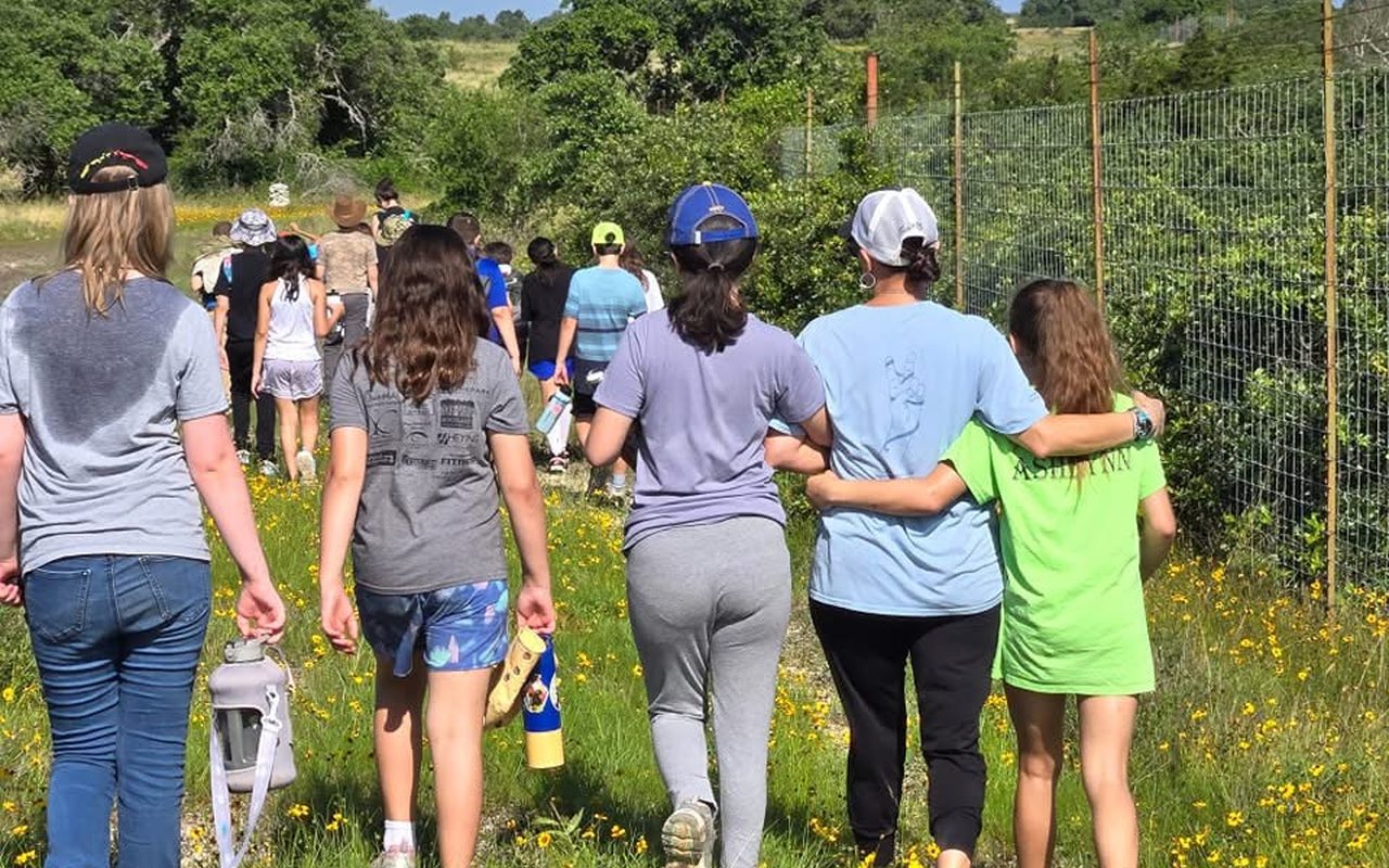 TriPoint students walking through a wildflower field with arms around each other.