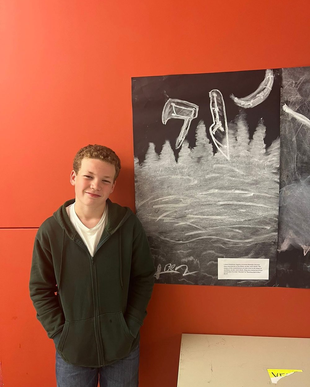 A TriPoint student standing beside their charcoal artwork on an orange wall.